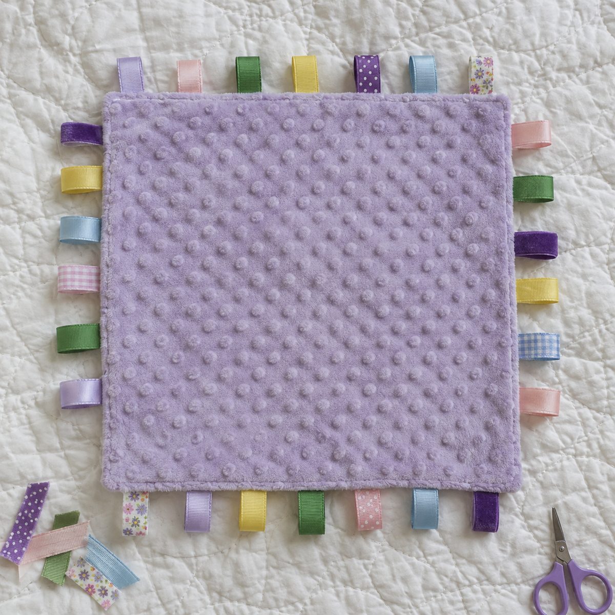 Taggie ribbon blanket with colorful ribbon loops around the edges