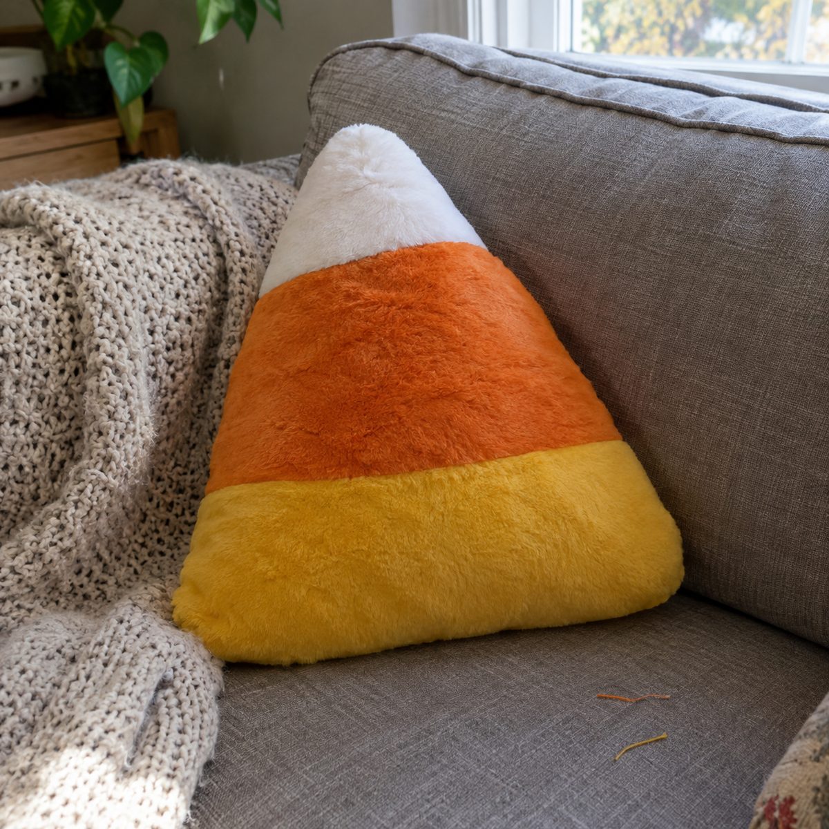 Candy corn pillow in white, orange, and yellow stripes on a gray sofa