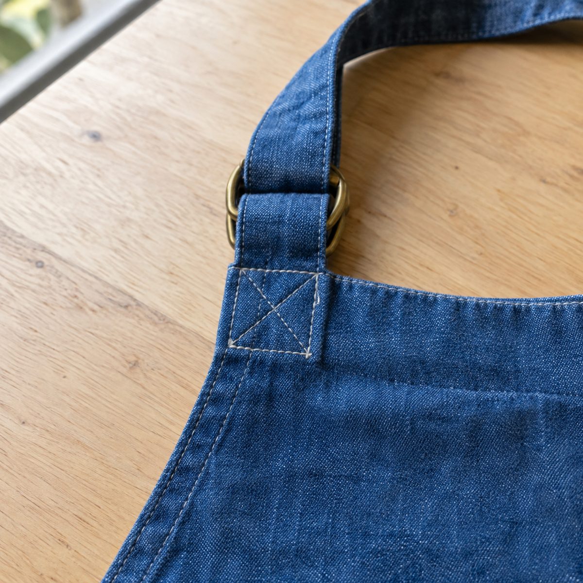 Adjustable apron neck strap threaded through brass D-rings with a box stitch