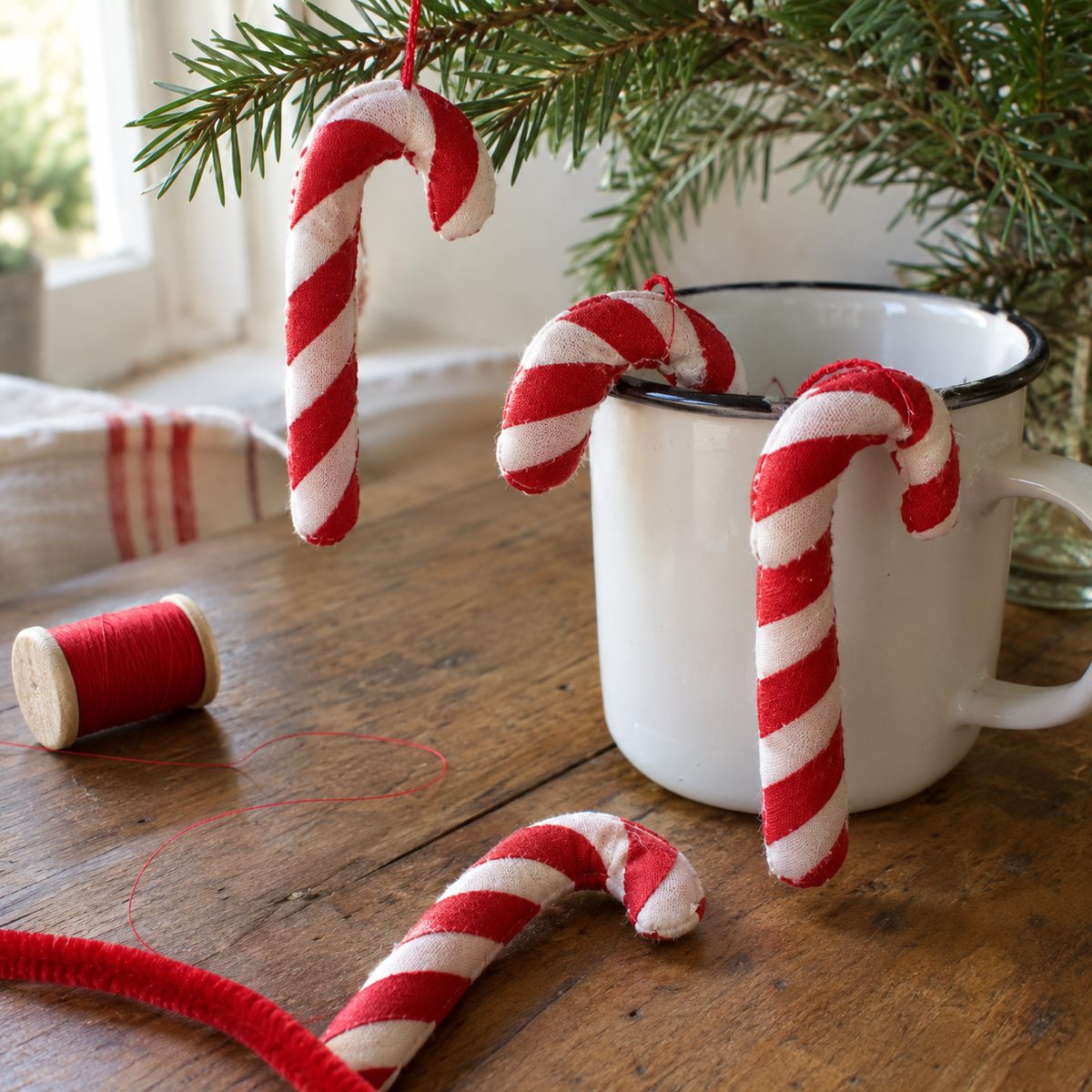 Fabric candy cane ornaments with spiral stripes hooked on a mug and pine branch