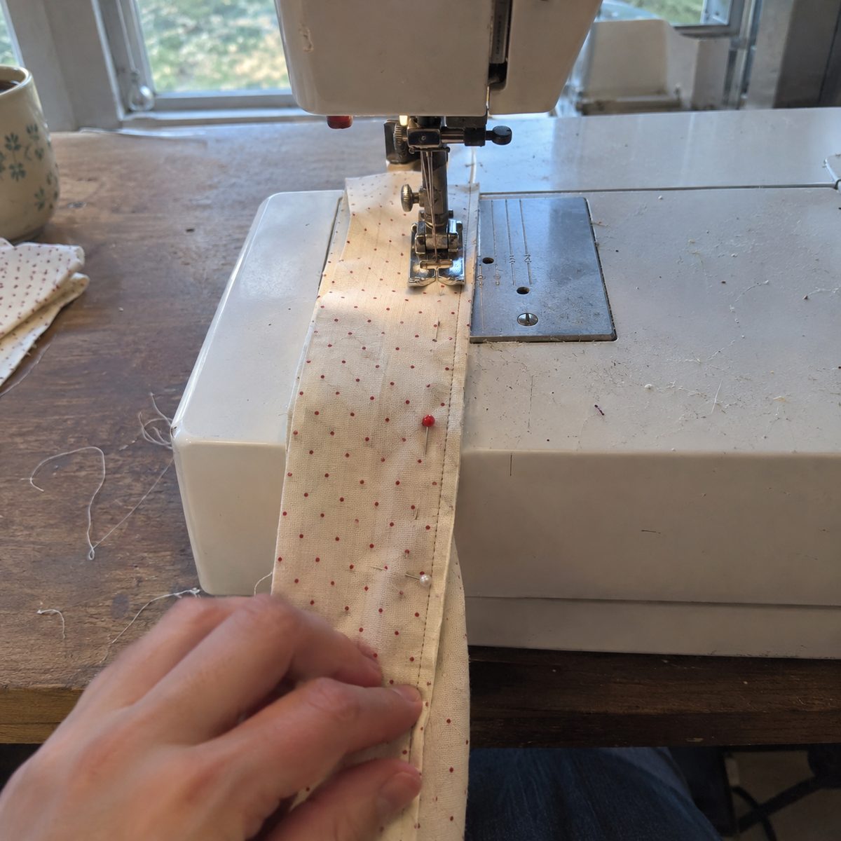 Folded pin dot cotton strip being sewn into a narrow tube on a sewing machine