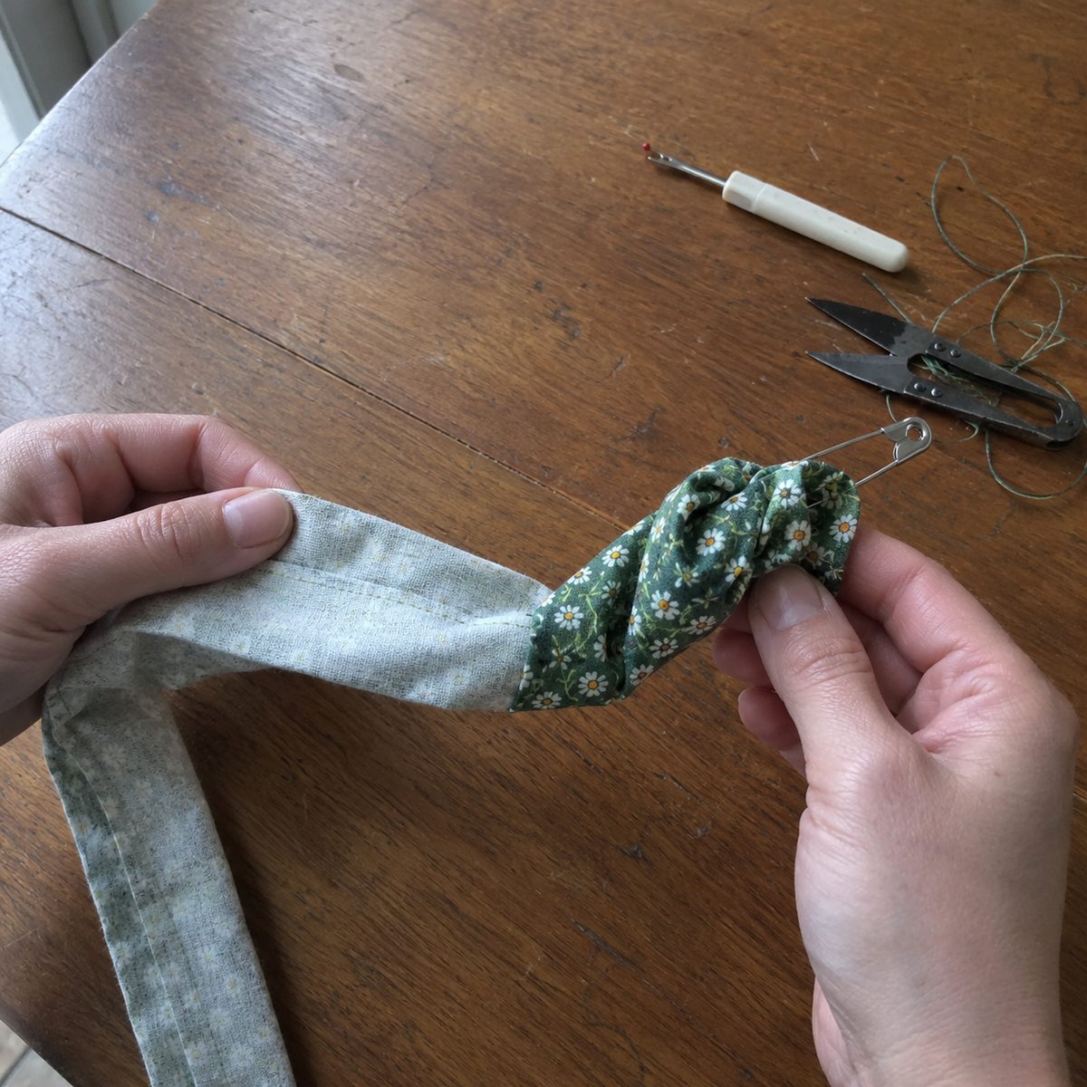 Hands using a safety pin to turn a narrow floral cotton tube right side out