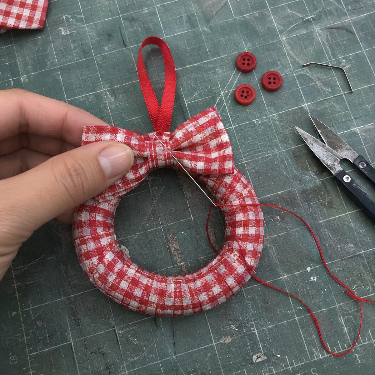 Sewing a small gingham bow over the join of a mini fabric wreath with the ribbon loop in place