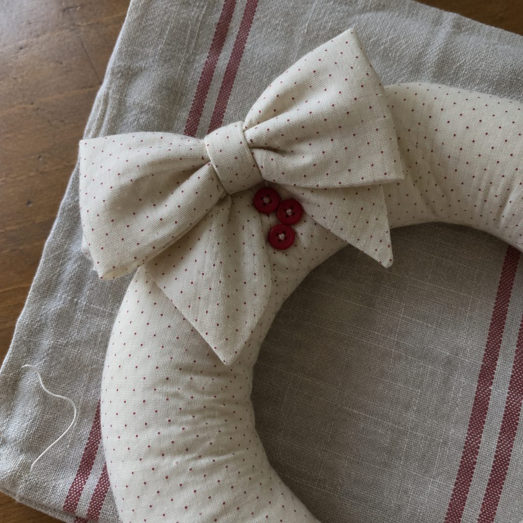 Close view of the bow and red button berries on a cream pin dot mini fabric wreath
