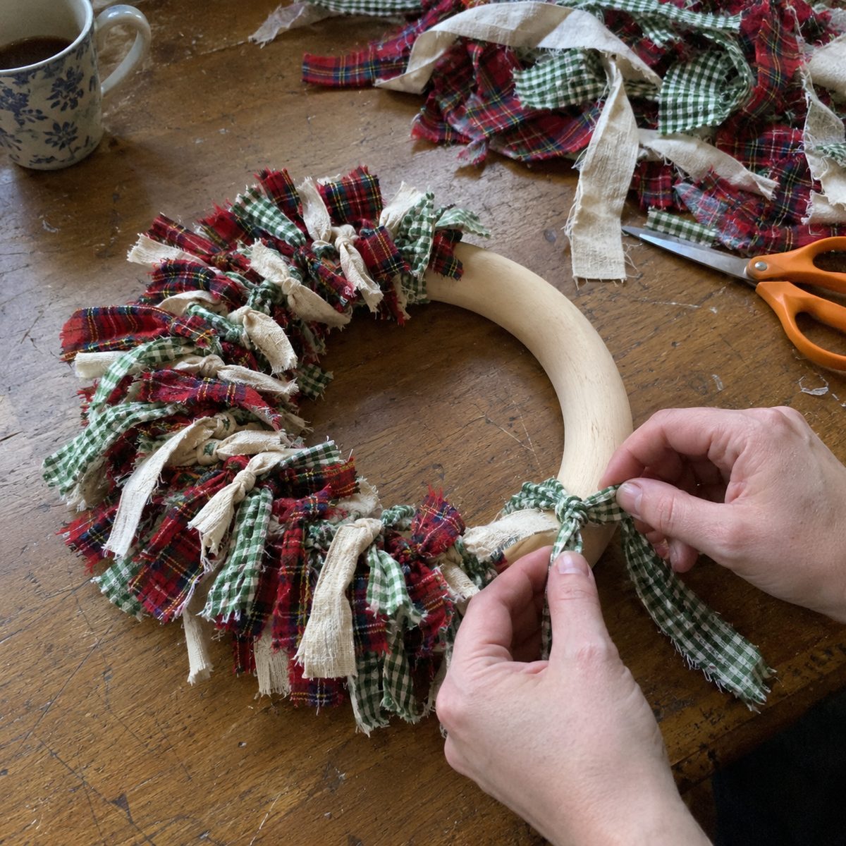 Tying torn plaid and gingham fabric strips onto a wooden ring to make a rag strip mini wreath