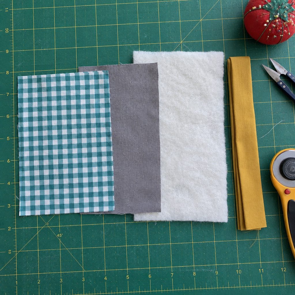 Cut fabric, batting and binding strip for a quilted mug rug on a cutting mat