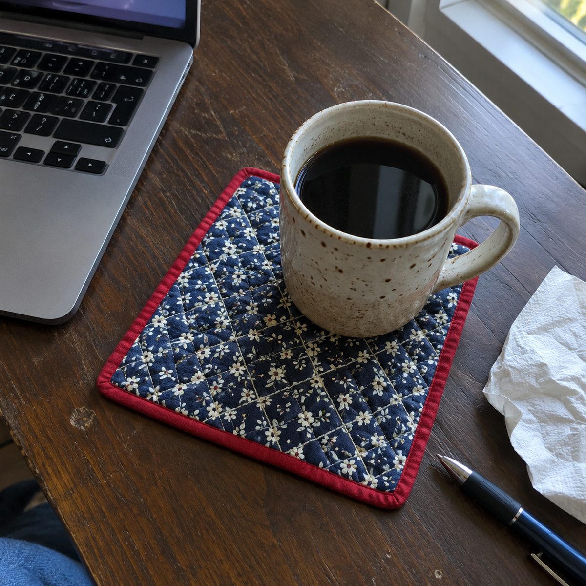 Finished bound quilted mug rug with a coffee mug on a desk