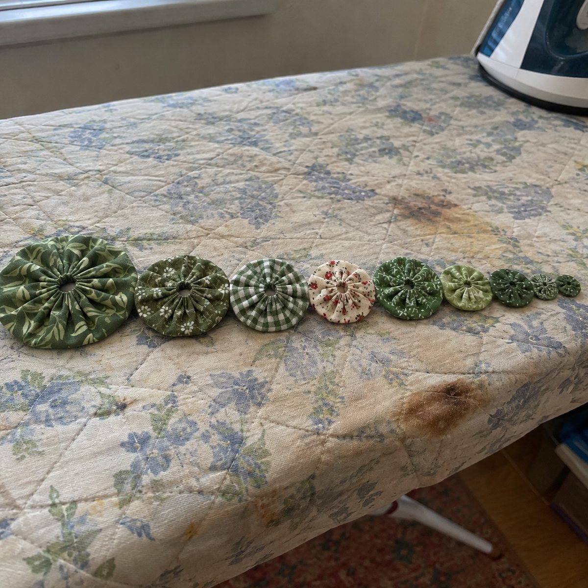 Close-up of nine finished fabric yo-yos in graduated sizes lined up biggest to smallest showing the gathered centers