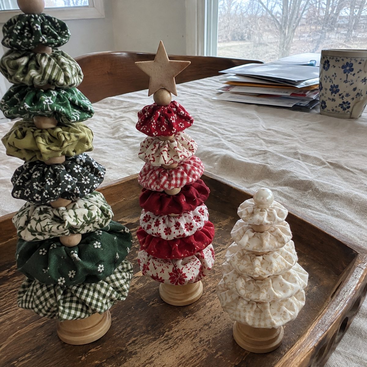Three fabric yo-yo Christmas trees in green, red and white, and cream prints in three heights on a wooden tray