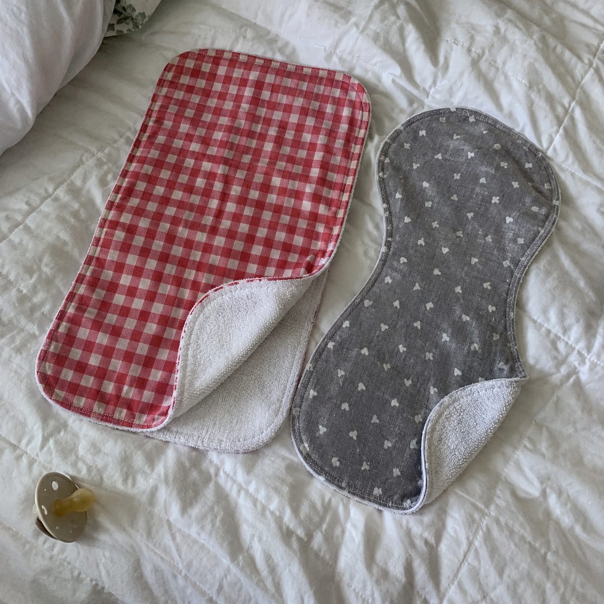 Rectangle and contoured handmade burp cloths side by side on a quilt showing terry backs and topstitching