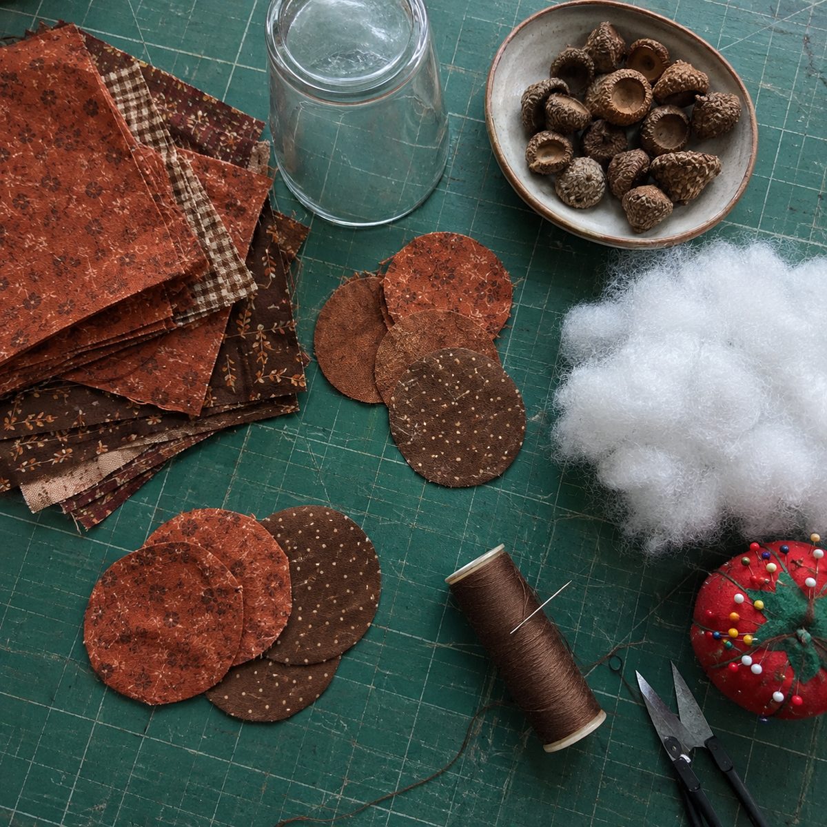 Fabric acorn supplies laid out on a cutting mat: cotton circles, fiberfill, acorn caps, thread
