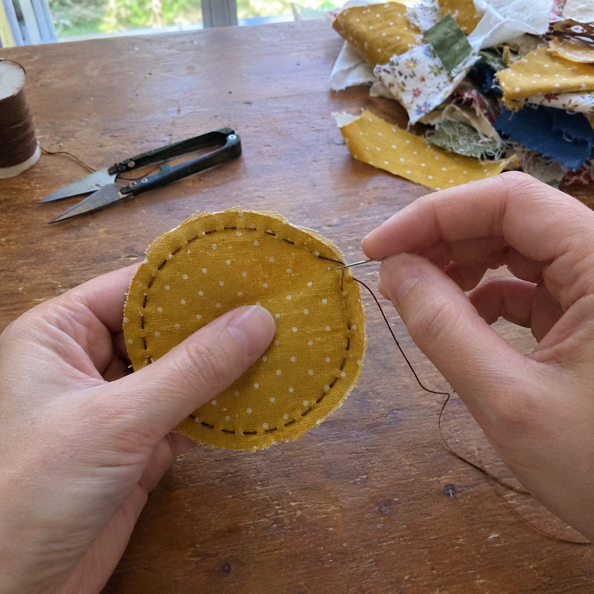 Hands sewing a running stitch around a circle of yellow dotted cotton for a fabric acorn