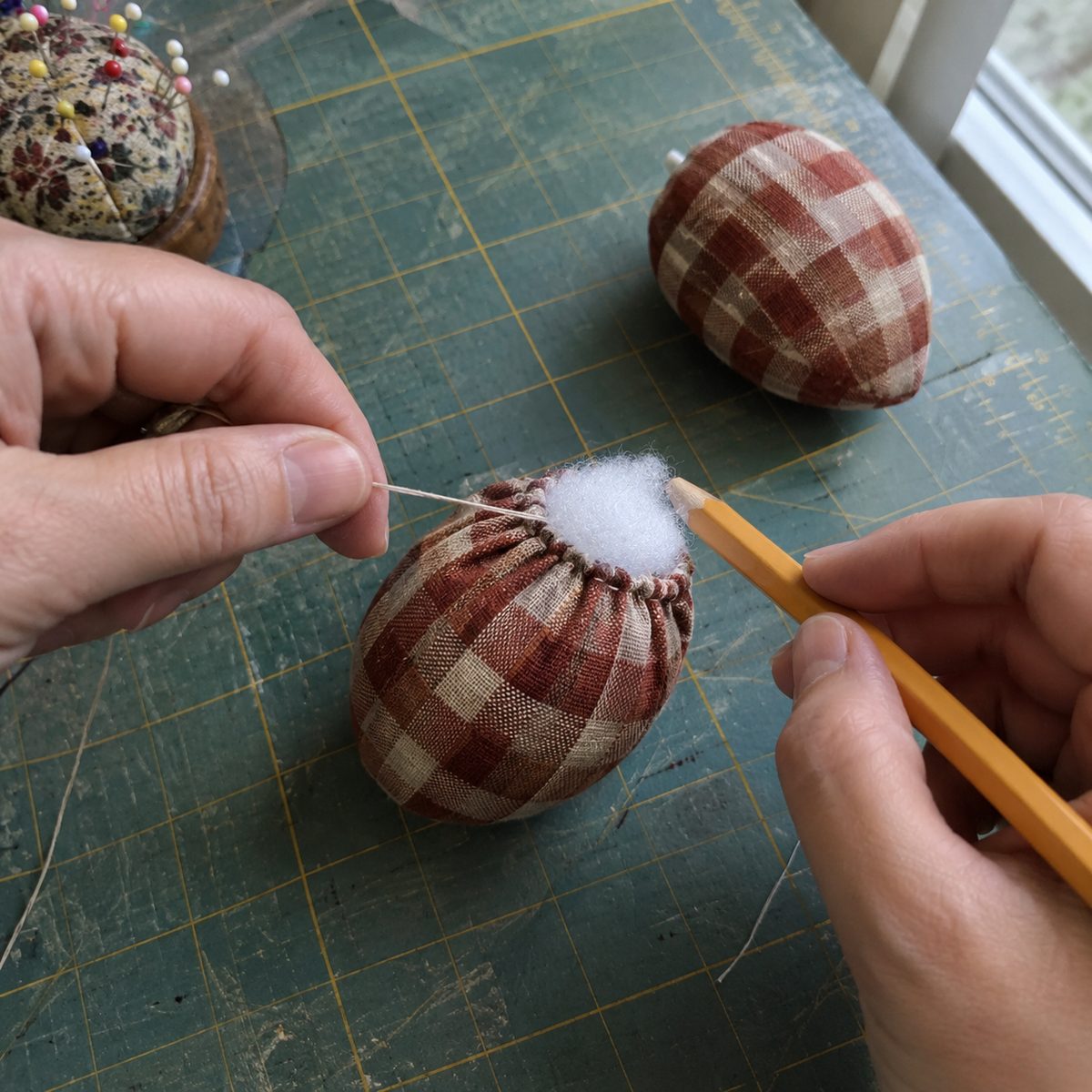 Hands gathering a stuffed plaid cotton circle closed to form a fabric acorn body
