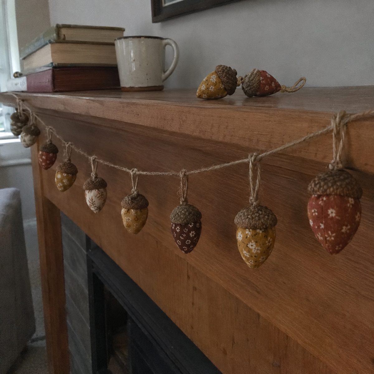 Garland of hand-sewn fabric acorns strung on jute twine across a wooden mantel