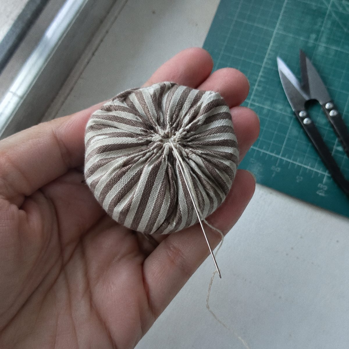 Close-up of the gathered top of a fabric acorn body showing the locking stitches before the cap goes on