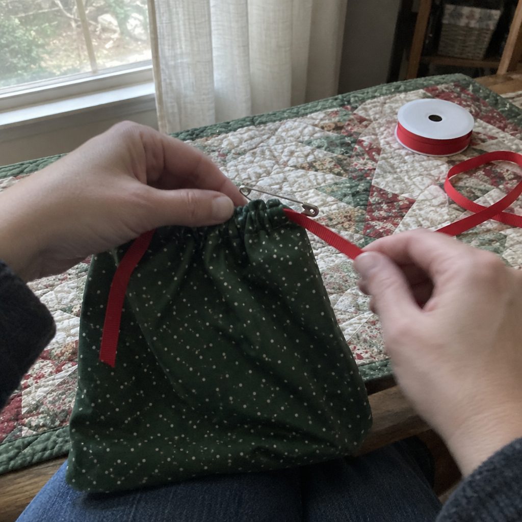 Threading a ribbon drawstring through a fabric gift bag casing with a safety pin