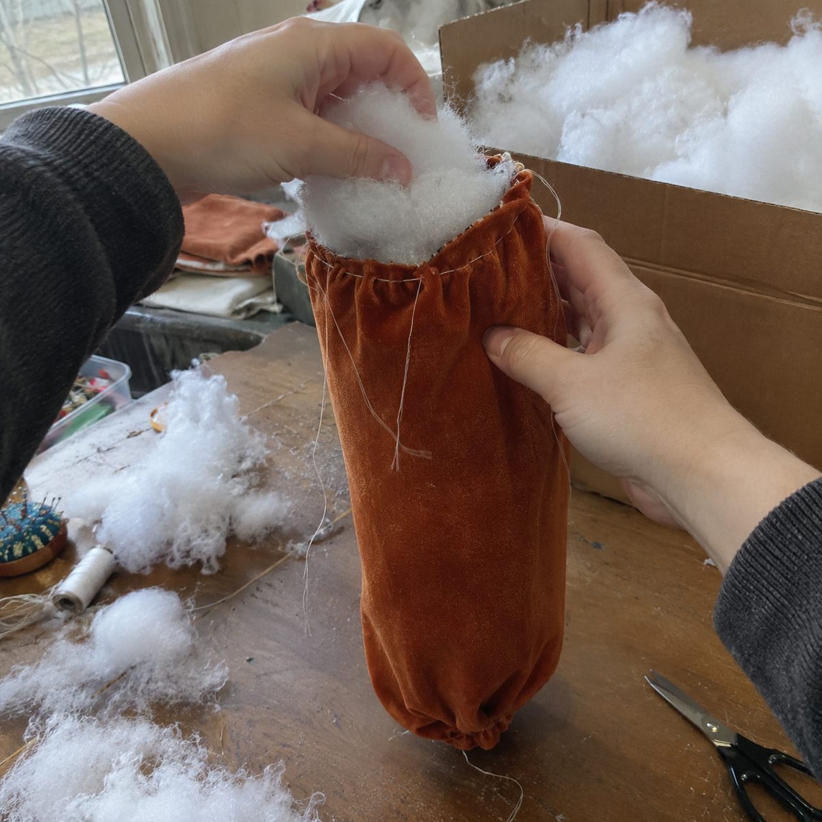 Stuffing a velvet fabric pumpkin with fiberfill before gathering the top closed