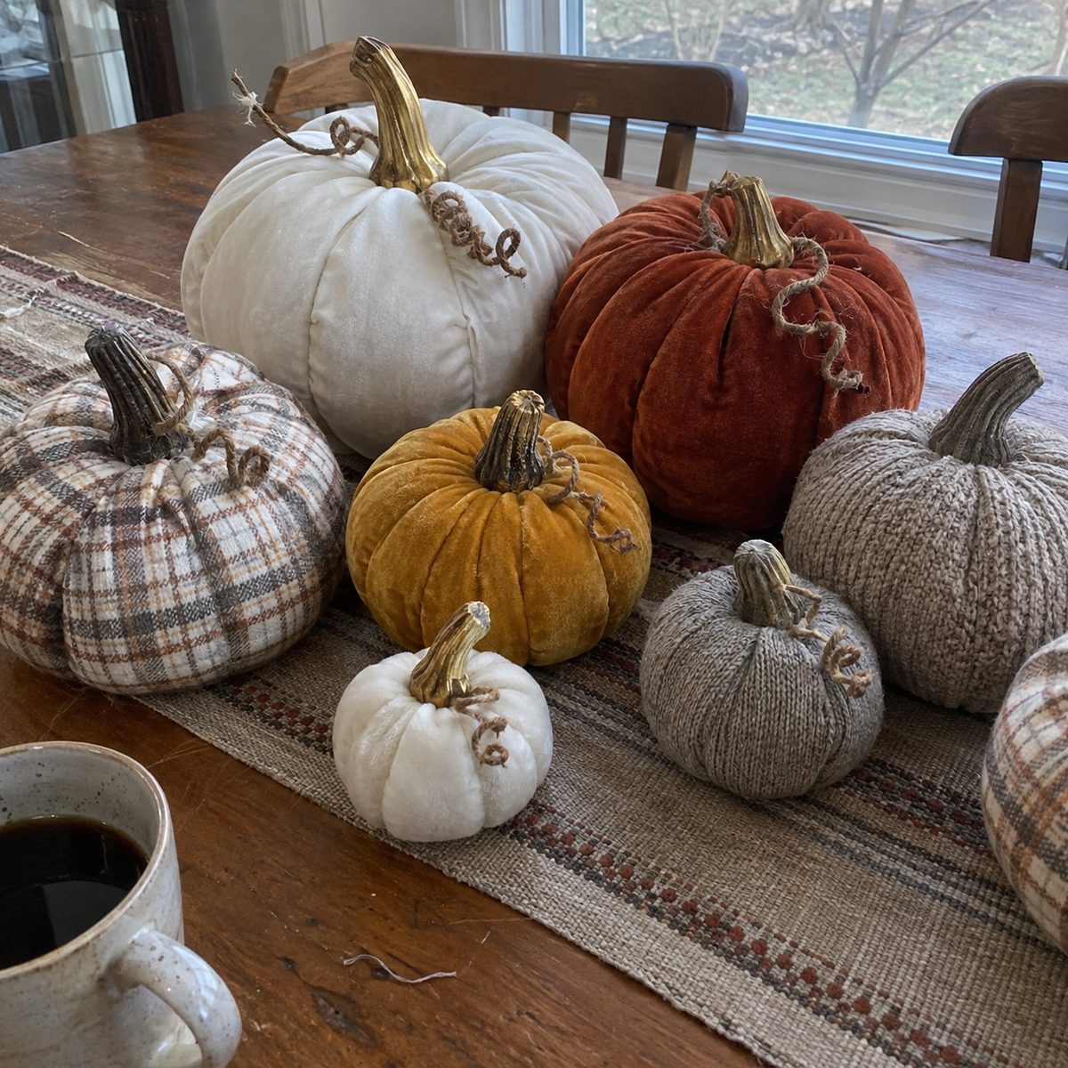 A batch of handmade fabric pumpkins in velvet, flannel and sweater knit on a table runner