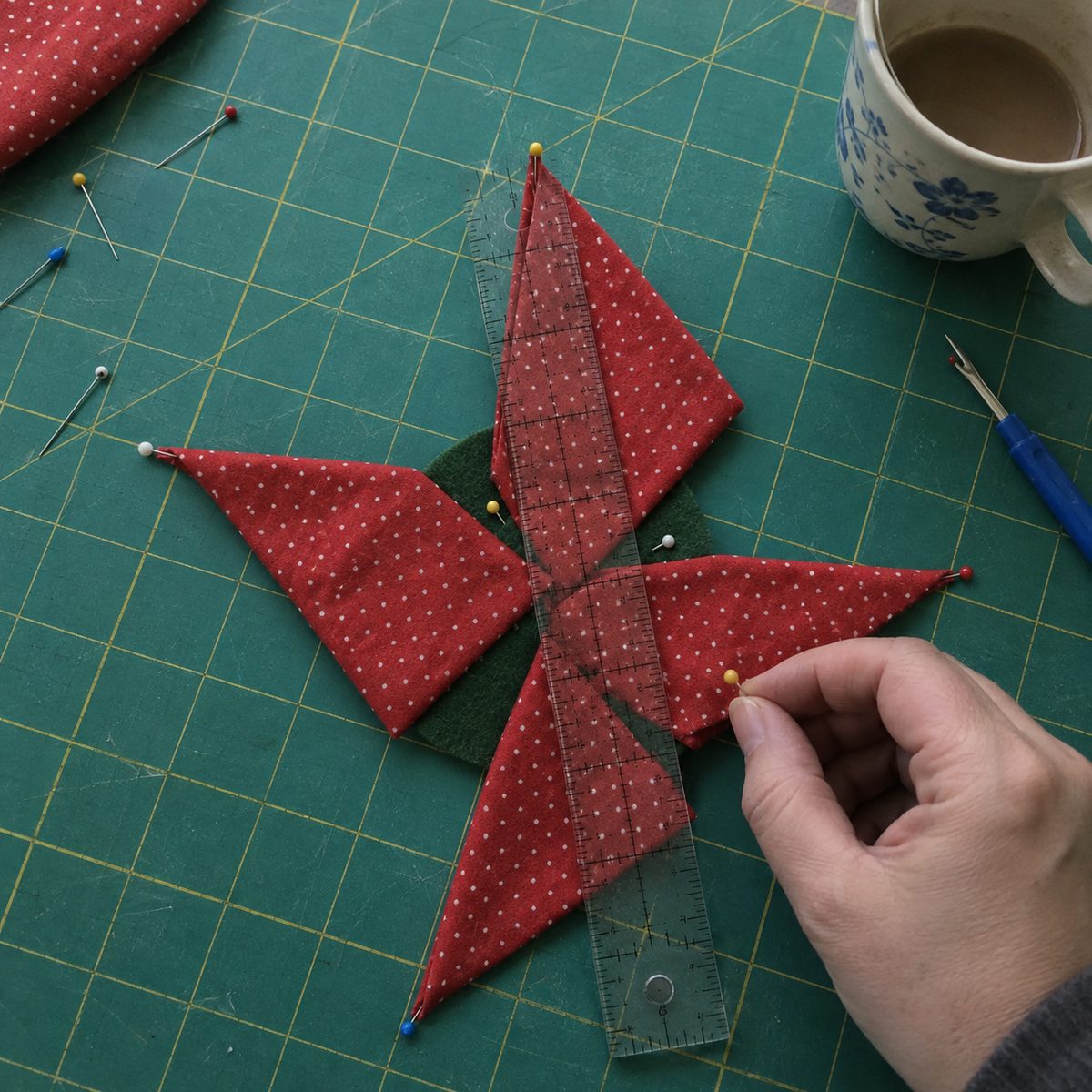 Four red folded points pinned in a pinwheel on a felt circle with a ruler checking the tips line up