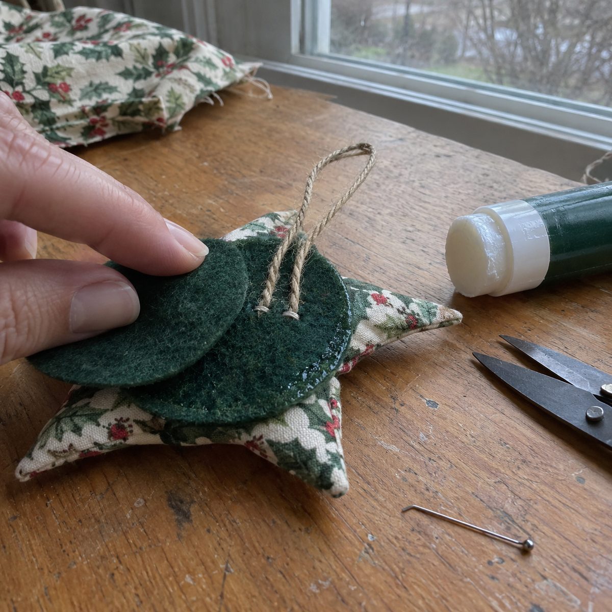 Back of a fabric star ornament with the twine loop ends stitched to felt and a cover circle being glued on