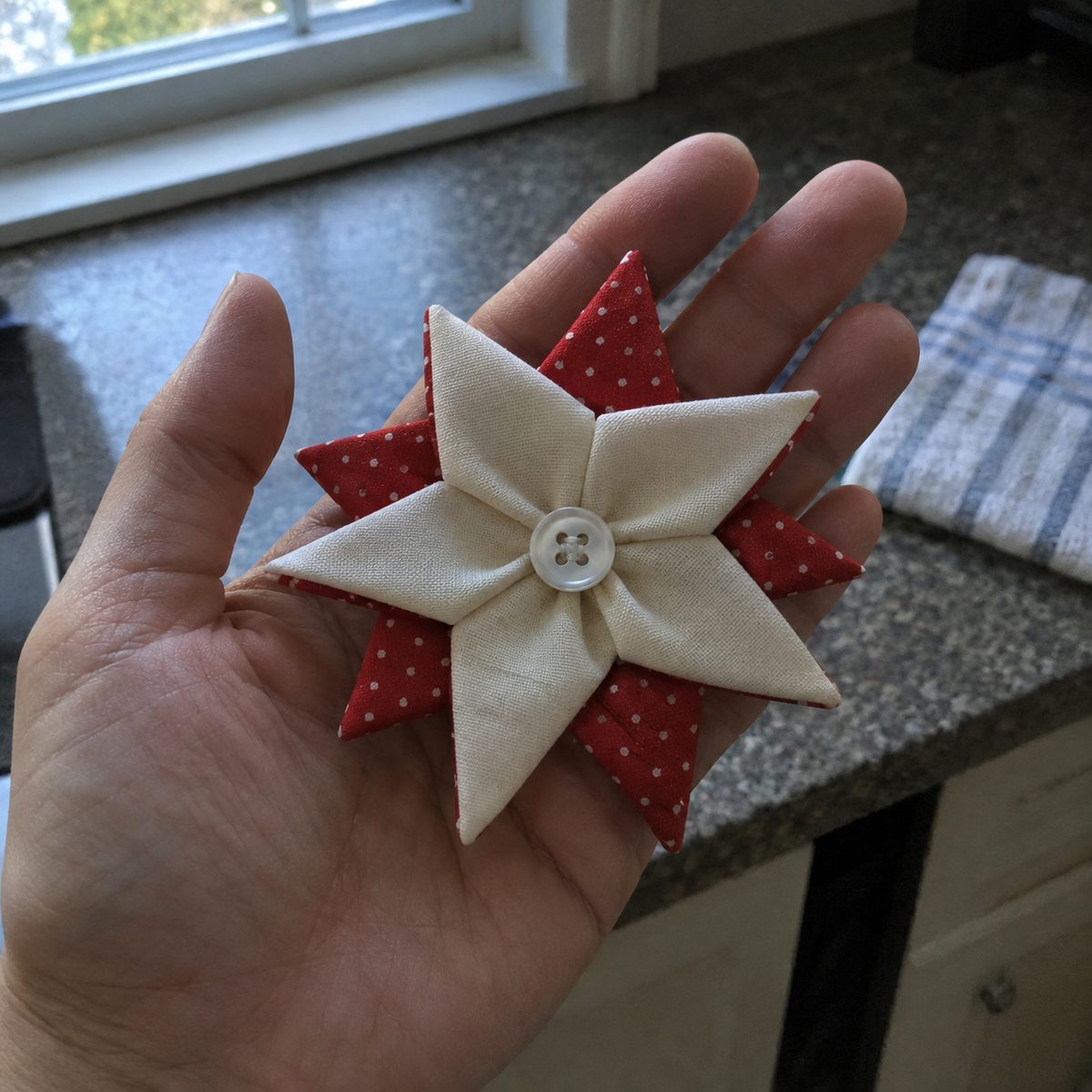Finished red and cream folded fabric star ornament with a button center held in an open hand