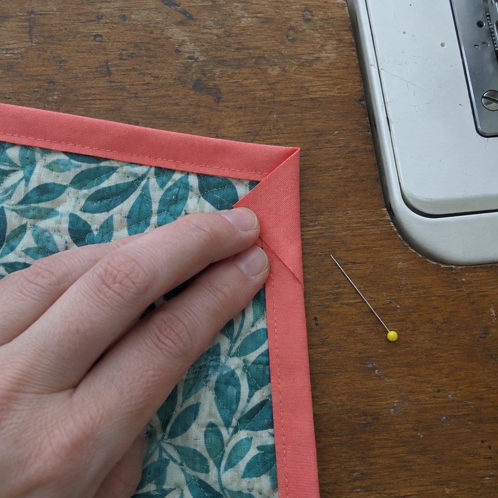 Folding a mitered corner while sewing double fold binding onto a quilted pot holder